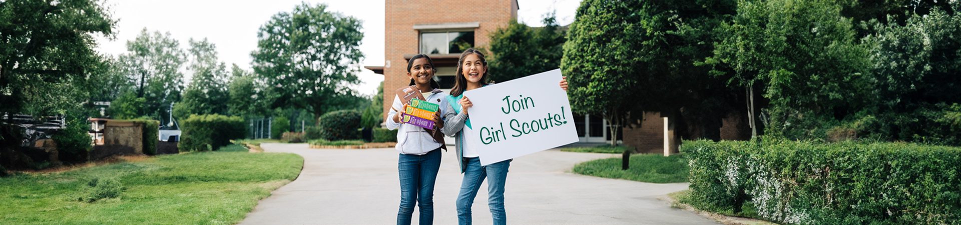  Two Girl Scouts standing on a sidewalk holding a sign that reads "Join Girl Scouts" 